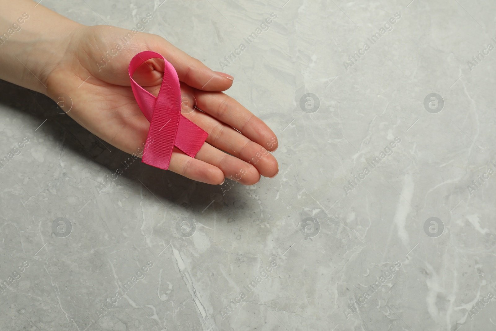 Photo of Breast cancer awareness. Woman with pink ribbon at grey marble table, top view. Space for text