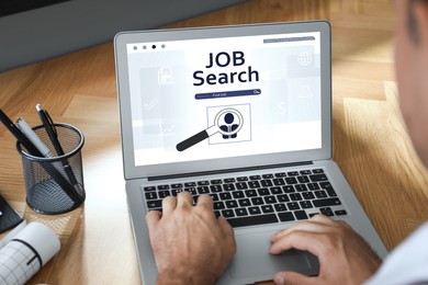 Man working with modern laptop at wooden table, closeup. Job search