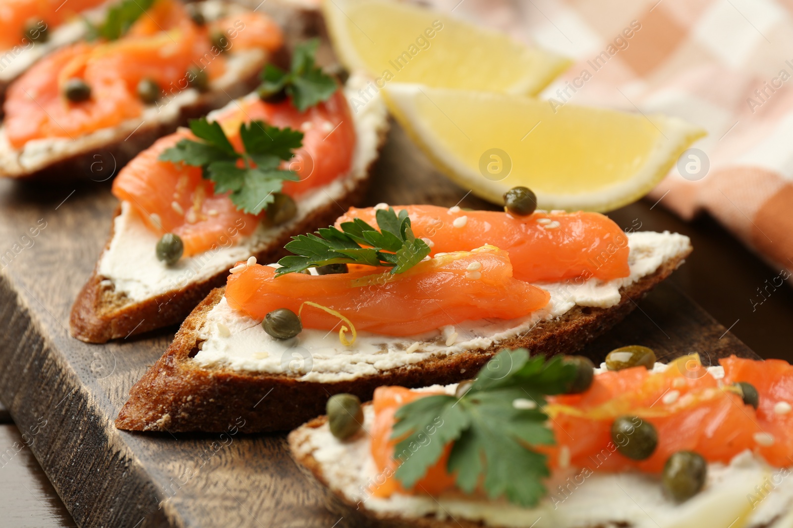 Photo of Tasty canapes with salmon, capers, lemon and cream cheese on wooden board, closeup