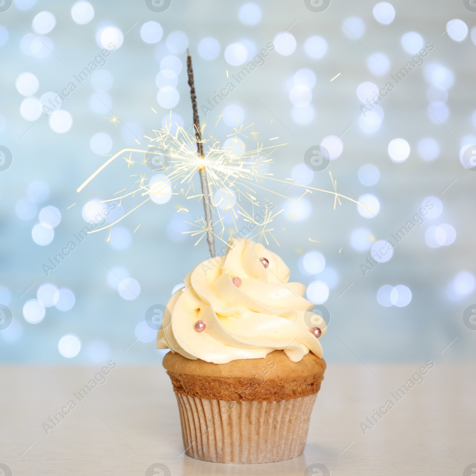 Image of Birthday cupcake with sparkler on table against blurred lights 