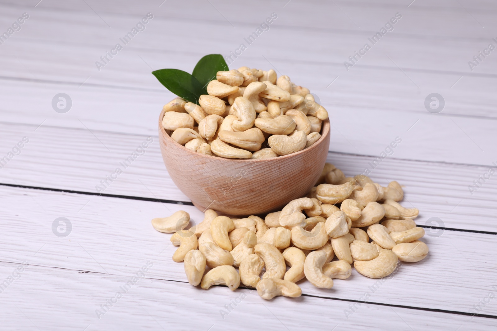 Photo of Tasty cashew nuts and green leaves on light wooden table