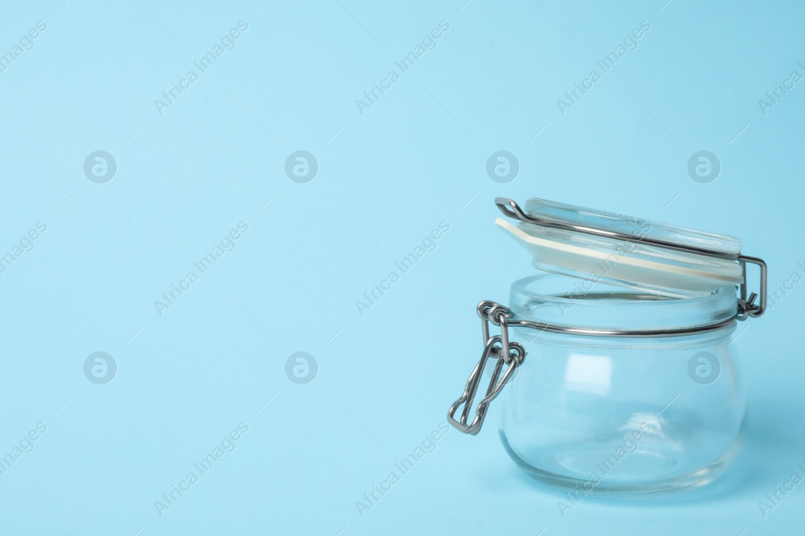 Photo of Open empty glass jar on light blue background, space for text