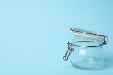 Photo of Open empty glass jar on light blue background, space for text