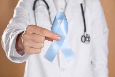 International Psoriasis Day. Doctor with light blue ribbon as symbol of support on beige background, closeup