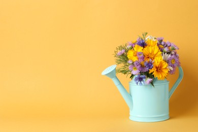 Light blue watering can with beautiful flowers on yellow background, space for text