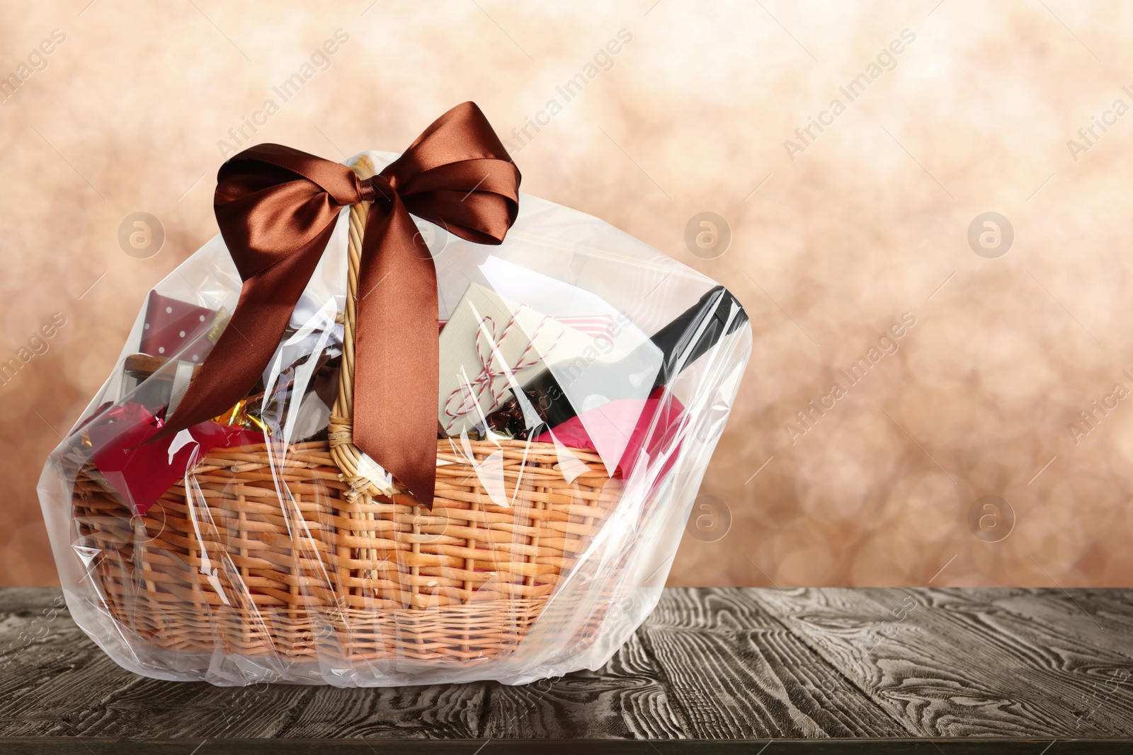 Image of Wicker basket full of gifts on wooden table against blurred background. Space for text