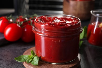 Photo of Jar of tasty tomato paste and ingredients on grey textured table, closeup