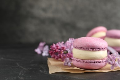 Photo of Delicious violet macaron and lilac flowers on black table, closeup. Space for text