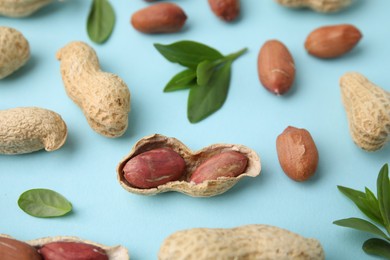 Photo of Fresh peanuts and leaves on light blue table, above view