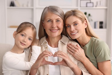 Photo of Three generations. Happy grandmother showing heart gesture with her daughter and granddaughter at home