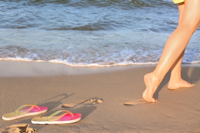 Photo of Closeup of woman and flip flops on sand near sea, space for text. Beach accessories