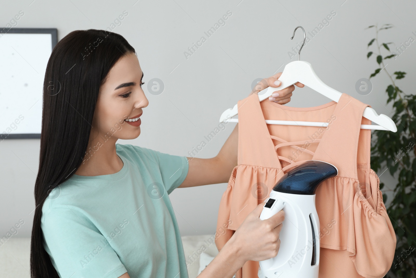 Photo of Woman steaming dress on hanger at home