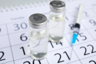 Photo of Vial and syringe on calendar, closeup. Vaccination and immunization