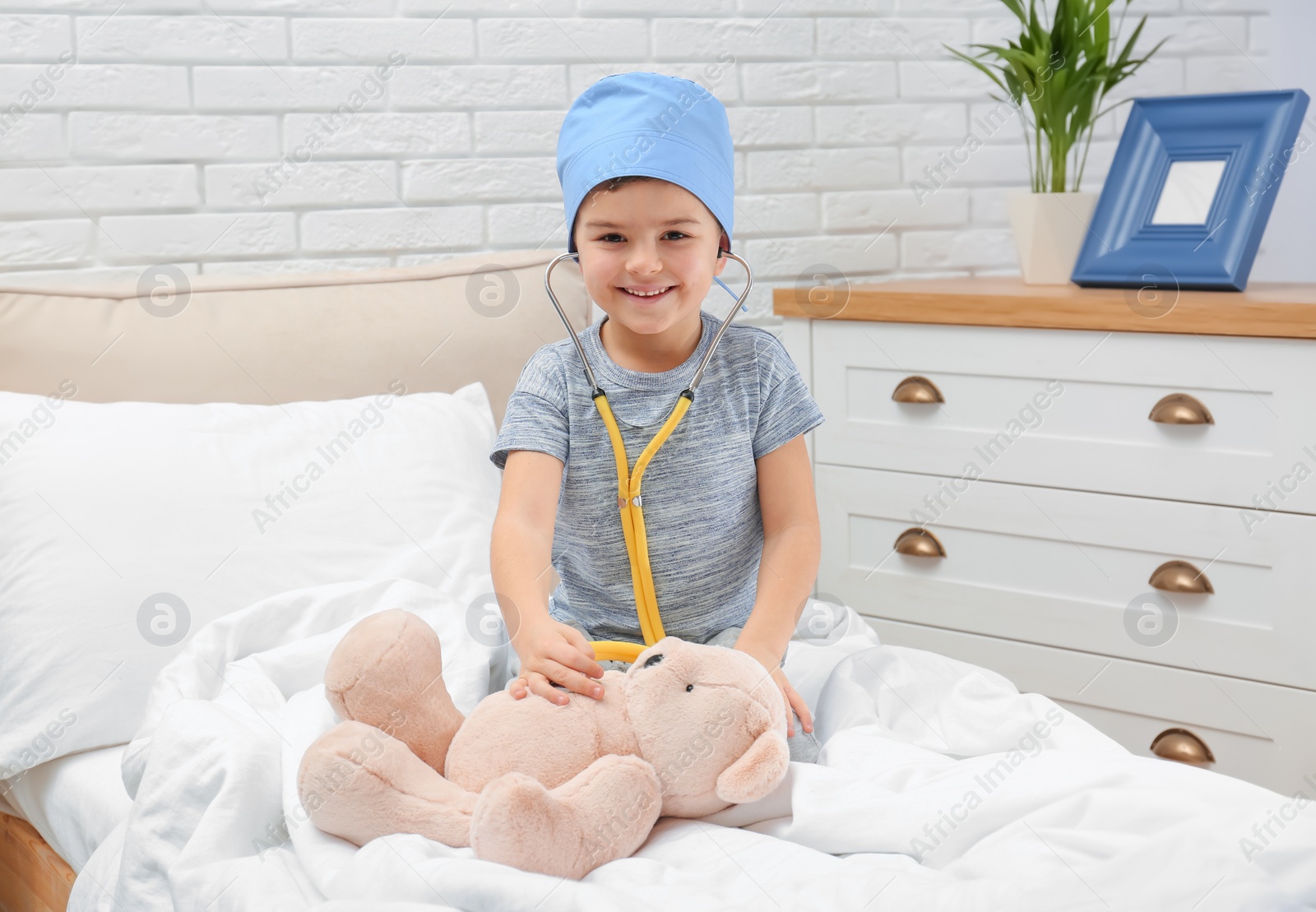 Photo of Cute child playing doctor with stuffed toy on bed in hospital ward