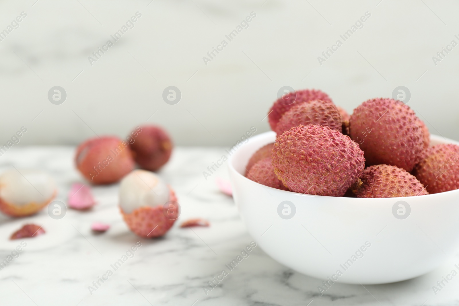 Photo of Fresh ripe lychee fruits in ceramic bowl on white marble table. Space for text