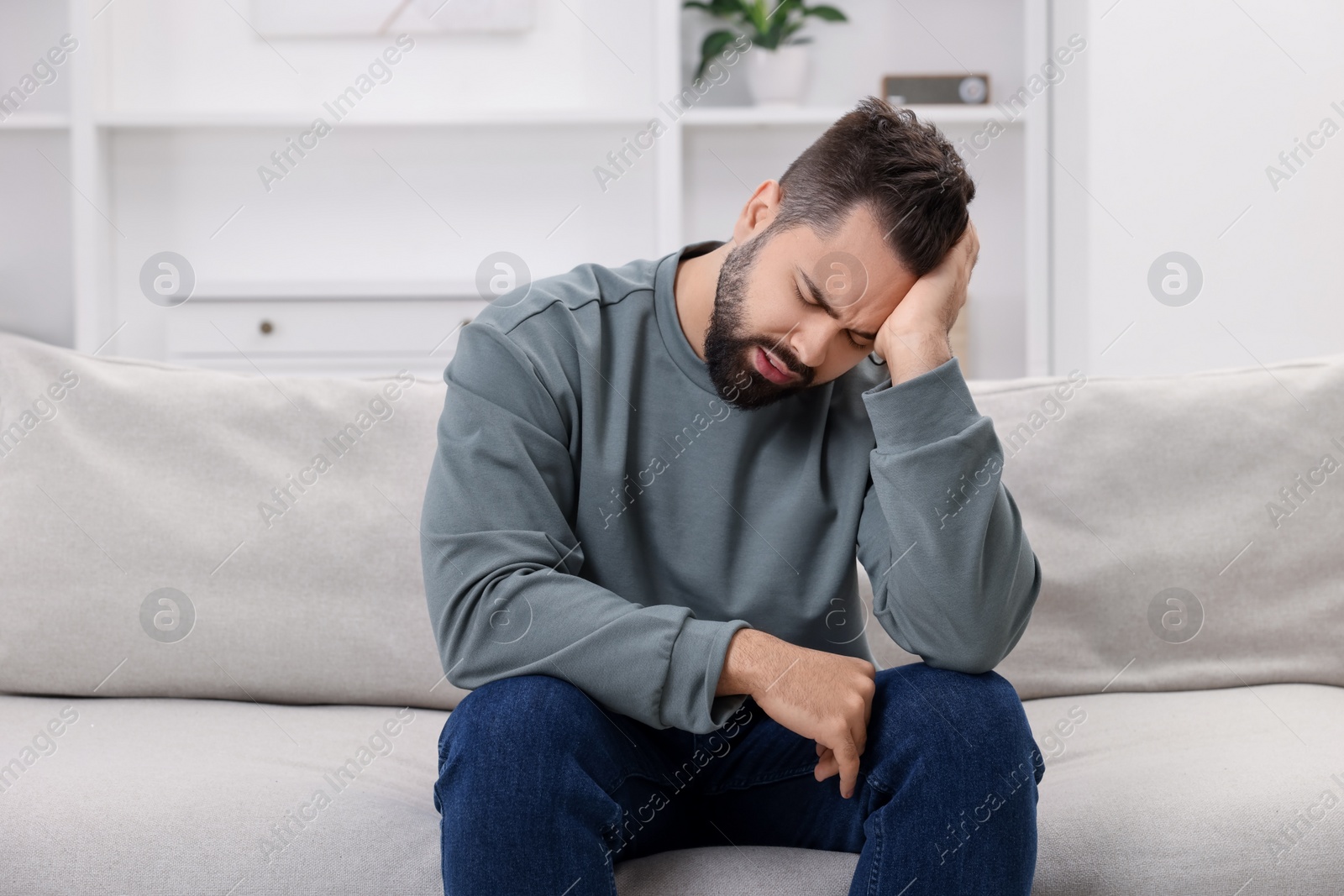 Photo of Man suffering from headache on sofa at home