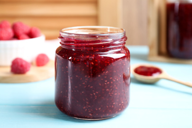 Photo of Delicious raspberry jam on light blue wooden table, closeup