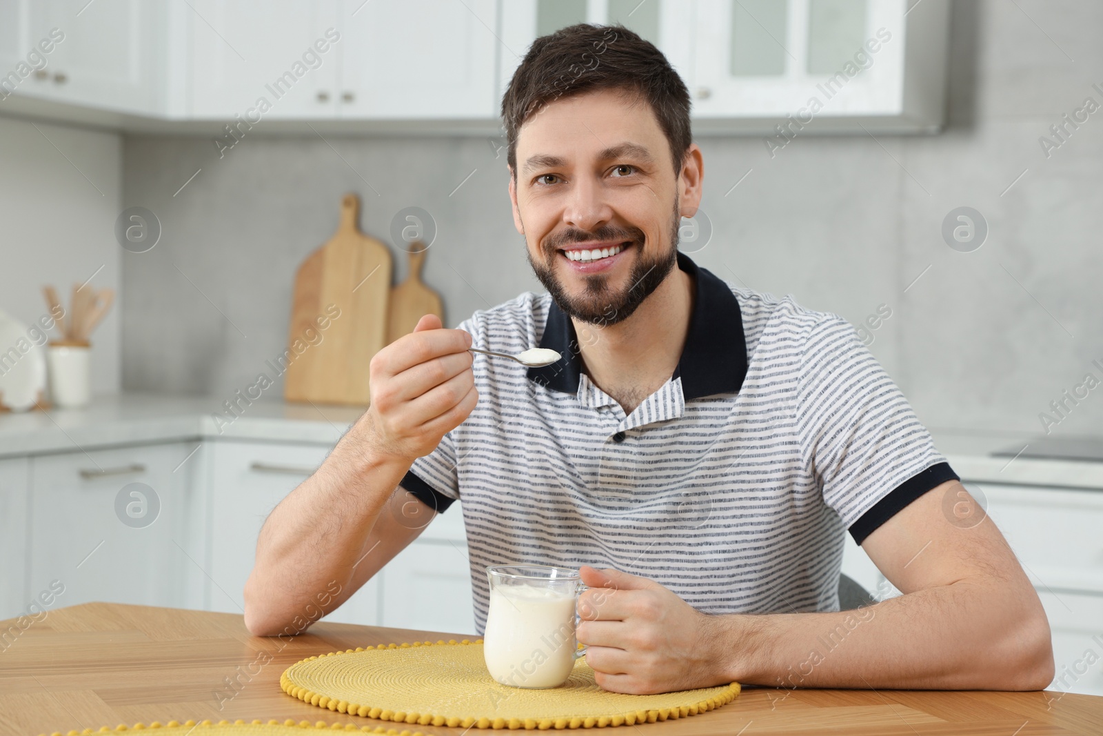 Photo of Handsome man with tasty yogurt at table in kitchen