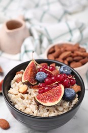 Bowl of oatmeal with berries, almonds and fig pieces on white marble table, closeup