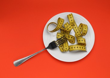 Photo of Plate, measuring tape and fork on red background, top view. Diet concept