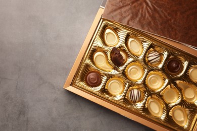 Partially empty box of chocolate candies on grey background, top view. Space for text