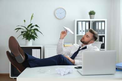 Photo of Lazy young man playing with paper plane in office