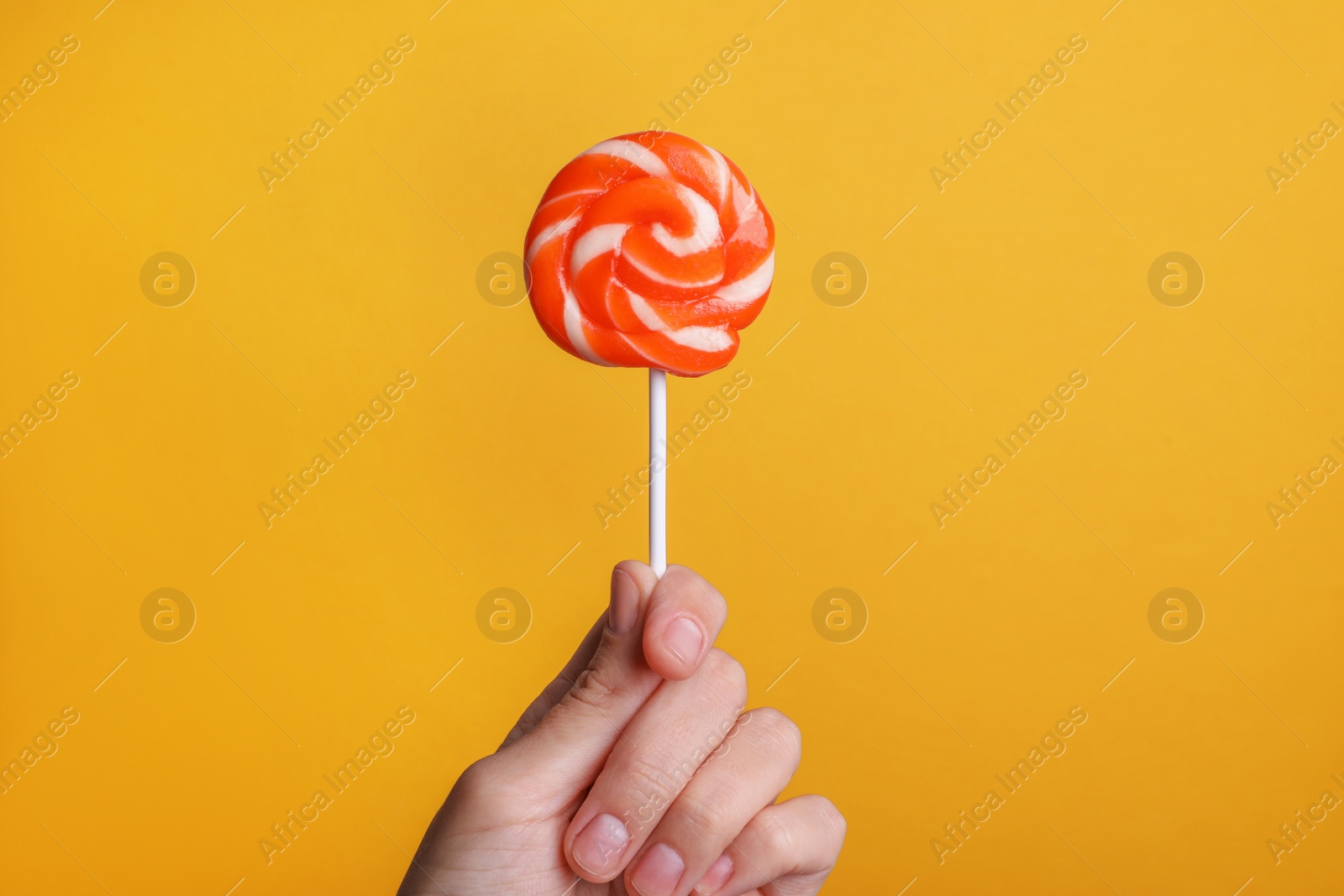 Photo of Woman holding bright tasty lollipop on orange background, closeup