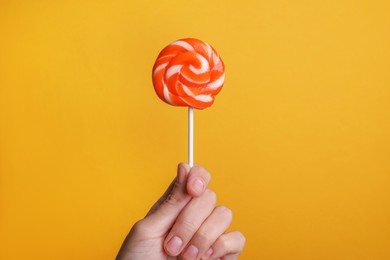 Photo of Woman holding bright tasty lollipop on orange background, closeup