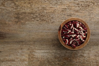 Photo of Bowl with dry kidney beans on old wooden table, top view. Space for text