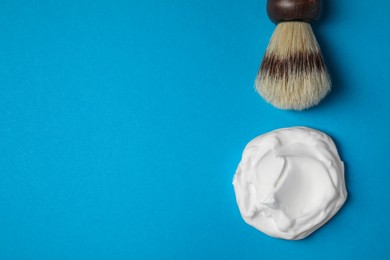 Sample of shaving foam and brush on blue background, flat lay. Space for text