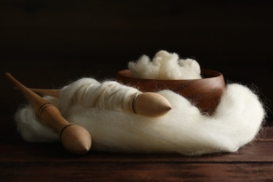 Photo of Soft white wool and spindles on wooden table, closeup