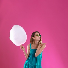 Happy young woman with cotton candy on pink background