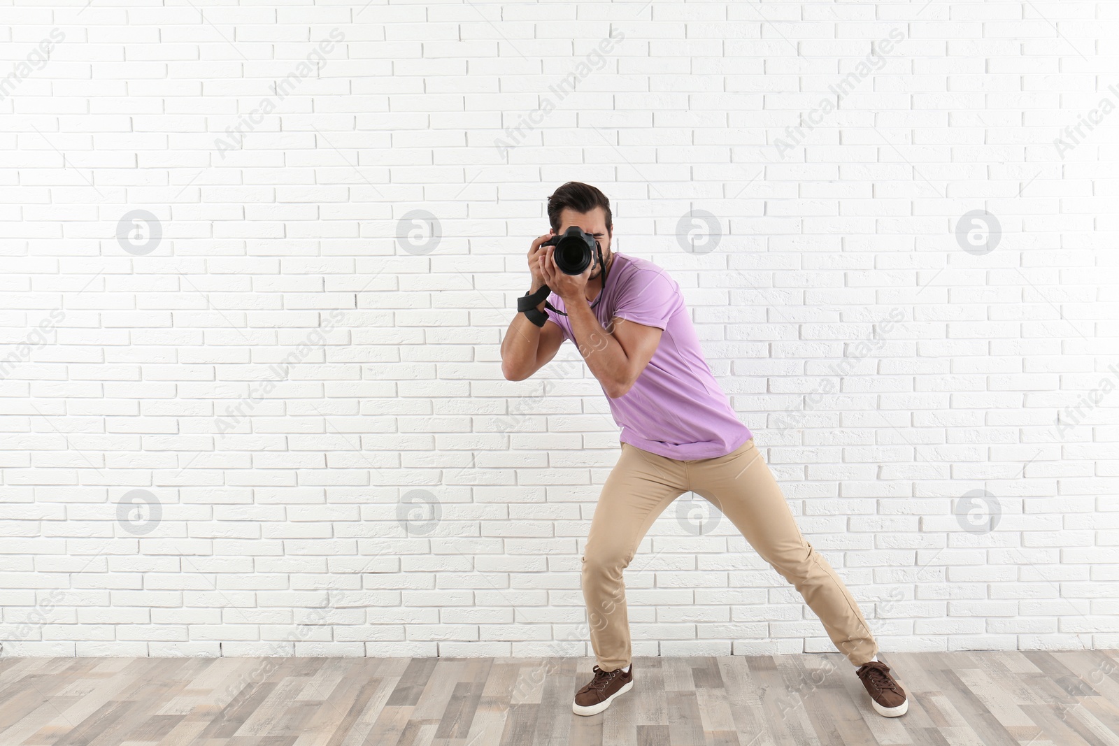 Photo of Young professional photographer taking picture near brick wall. Space for text