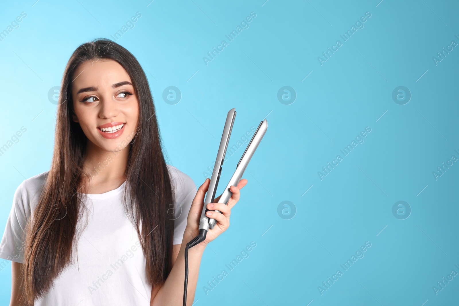 Photo of Happy woman with hair iron on color background. Space for text