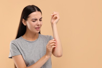 Photo of Suffering from allergy. Young woman scratching her arm on beige background. Space for text