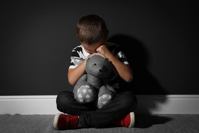 Photo of Scared little boy with toy near black wall. Domestic violence concept