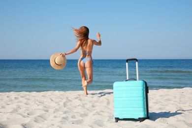 Photo of Woman in bikini running to sea and suitcase on beach, back view