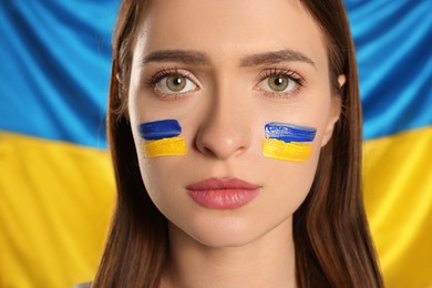 Photo of Young woman with face paint near Ukrainian flag, closeup
