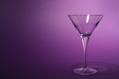 Photo of Elegant empty martini glass on purple background. Space for text