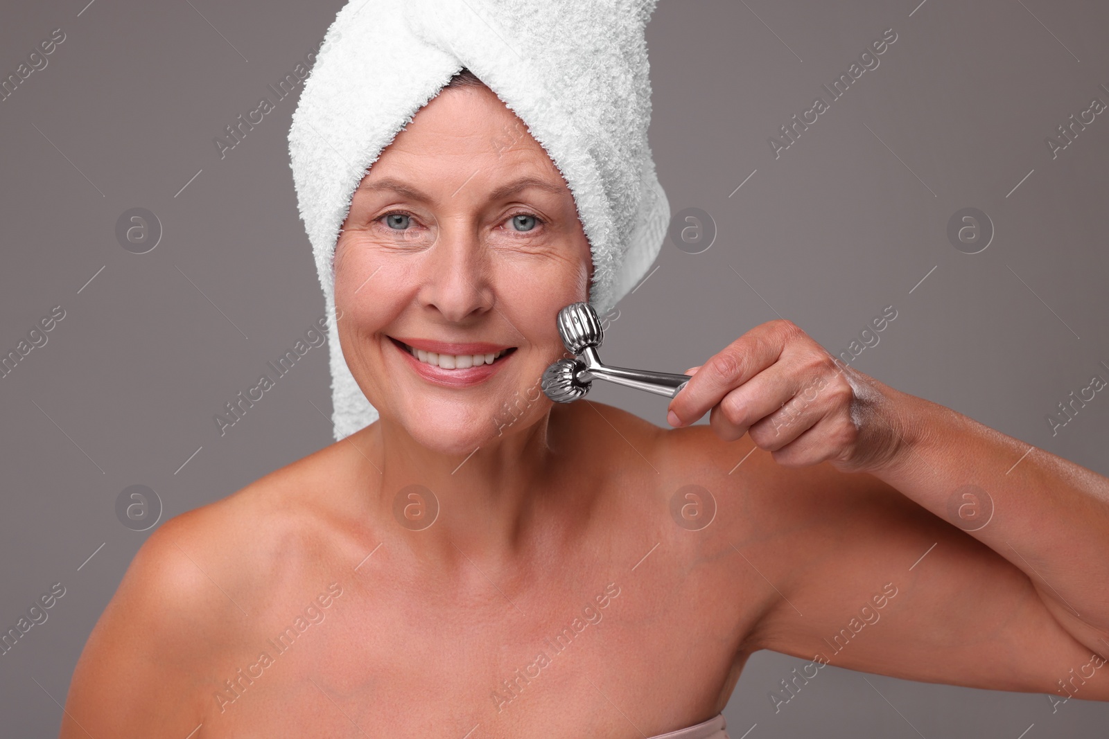 Photo of Woman massaging her face with metal roller on grey background