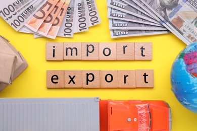 Words Import and Export made of wooden cubes, toy truck and banknotes on yellow background, flat lay
