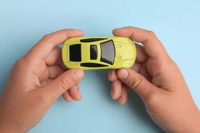 Photo of Child holding toy car on light blue background, top view