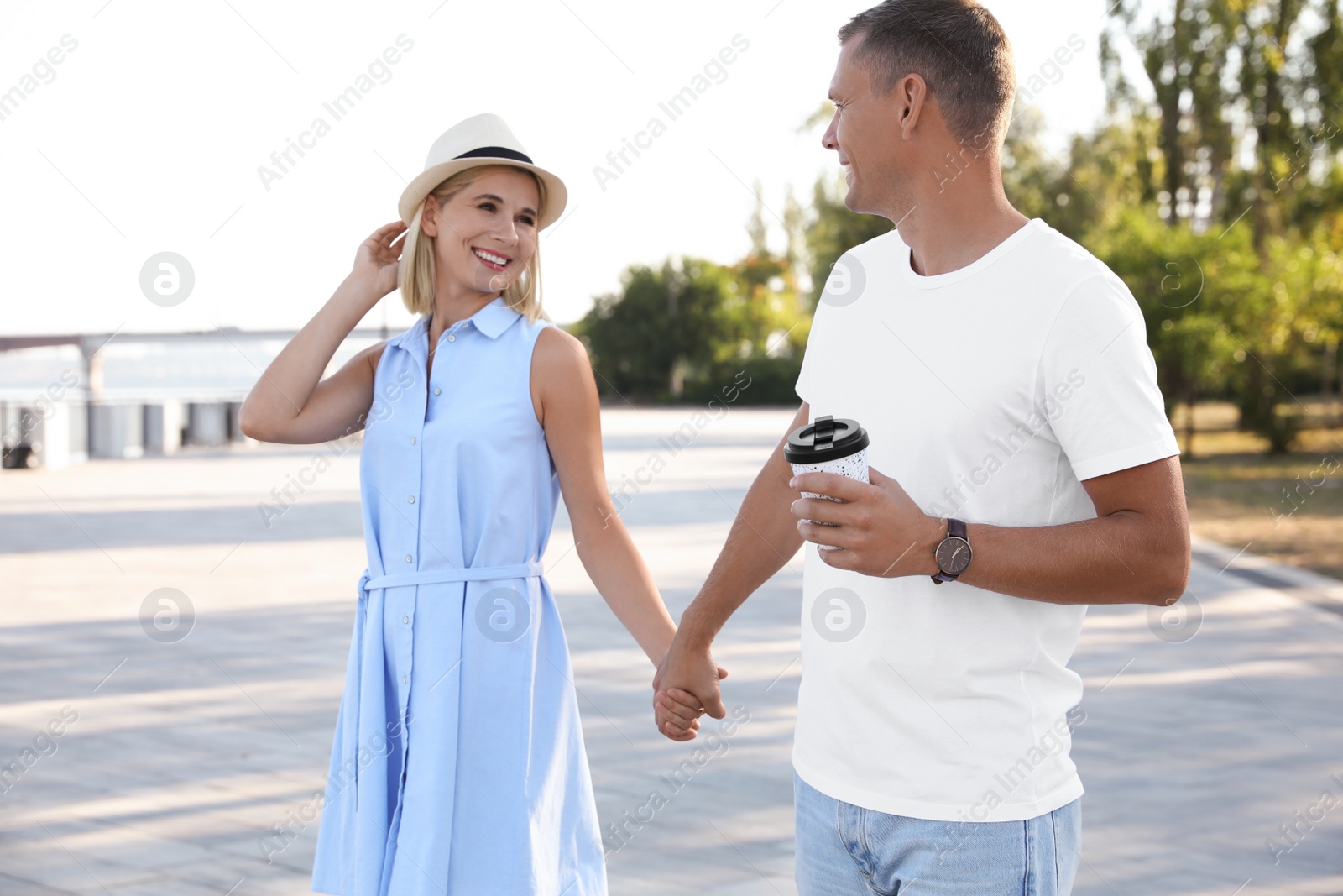 Photo of Happy couple with drink walking along city street on summer day