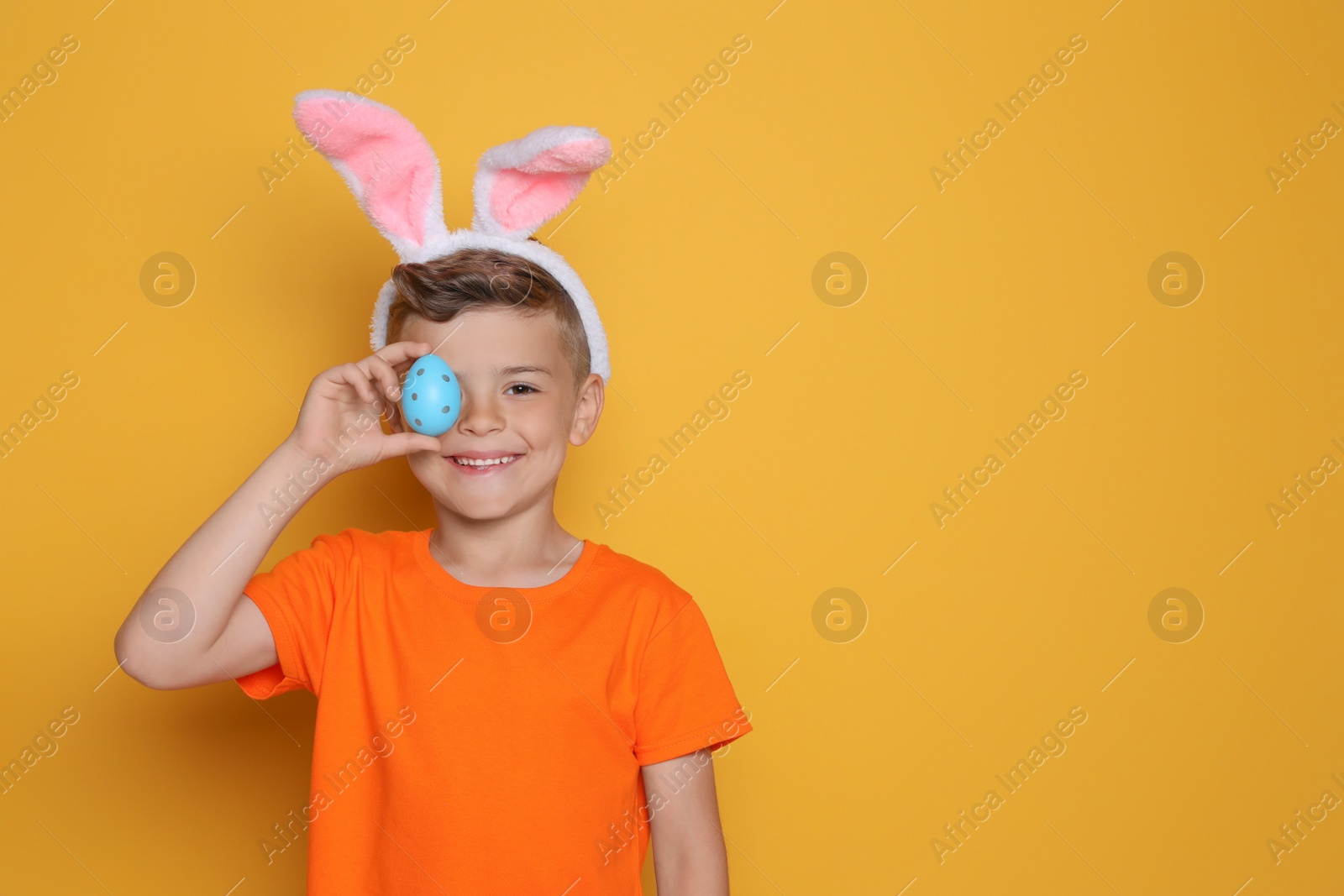 Photo of Cute little boy in bunny ears holding Easter egg on yellow background. Space for text