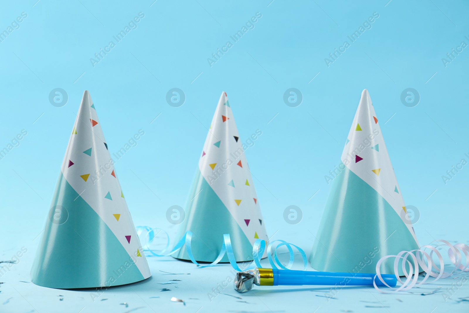 Photo of Bright party hats, horn, serpentine streamers and confetti on light blue background