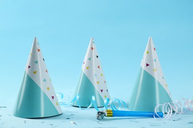 Photo of Bright party hats, horn, serpentine streamers and confetti on light blue background