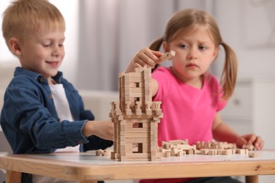 Little girl and boy playing with wooden tower at table indoors, selective focus. Children's toy