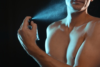 Photo of Young man spraying perfume on black background, closeup