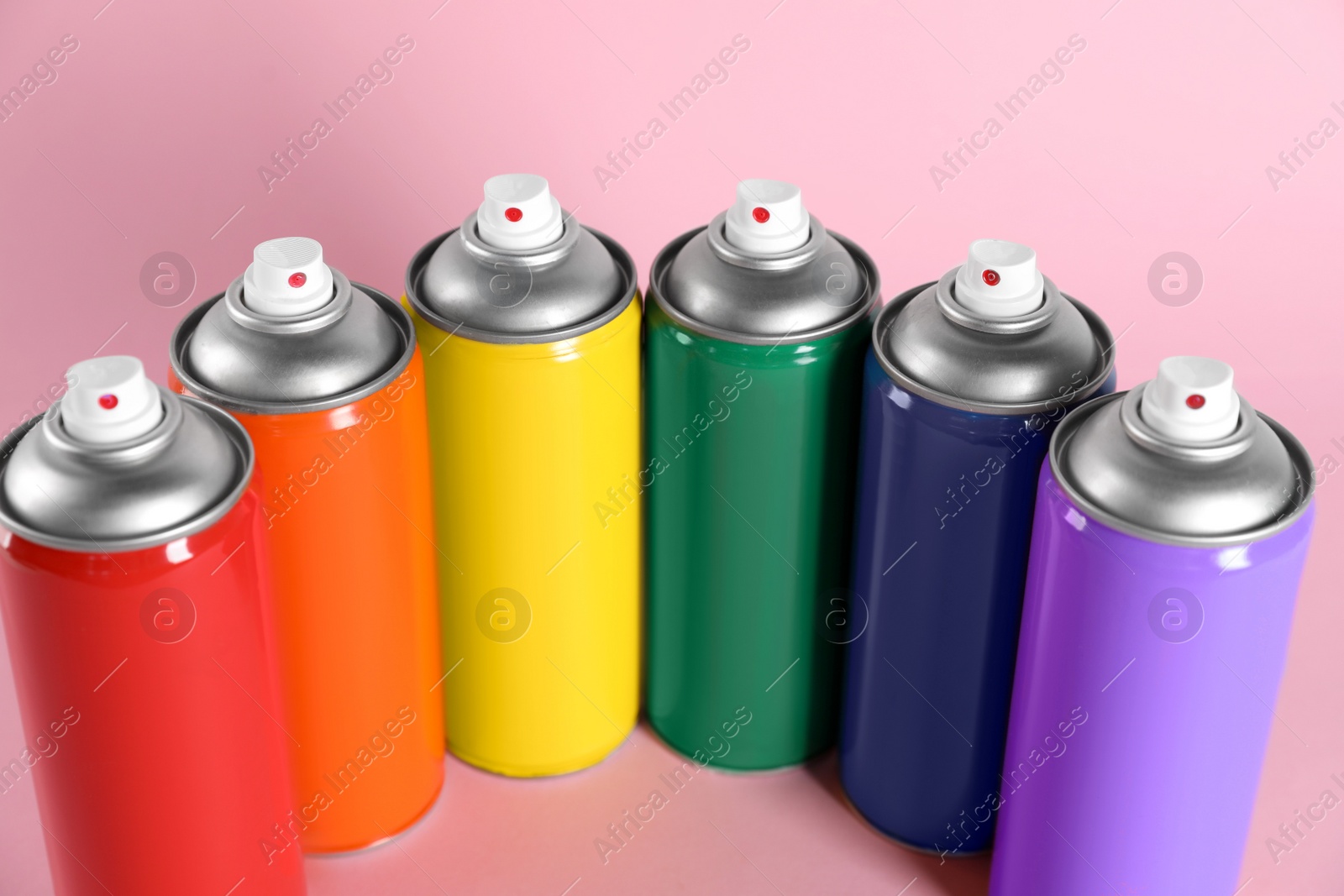 Photo of Colorful cans of spray paints on pink background