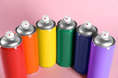 Photo of Colorful cans of spray paints on pink background